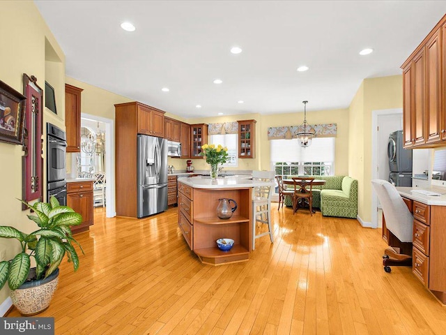 kitchen featuring stacked washer / dryer, appliances with stainless steel finishes, light wood-type flooring, pendant lighting, and a kitchen island