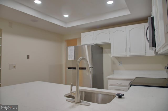 kitchen with stainless steel fridge, stove, a raised ceiling, sink, and white cabinets