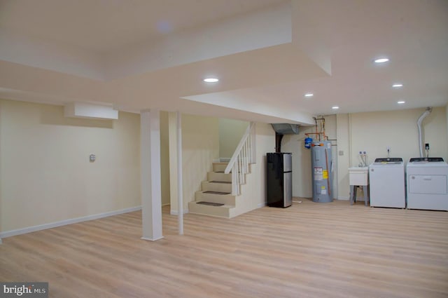 basement featuring sink, light wood-type flooring, washing machine and dryer, and water heater