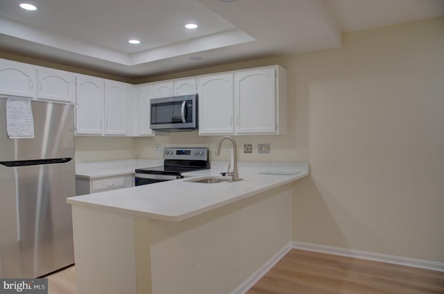 kitchen featuring white cabinetry, sink, stainless steel appliances, a raised ceiling, and kitchen peninsula