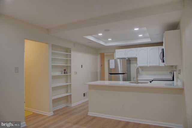 kitchen with kitchen peninsula, appliances with stainless steel finishes, light wood-type flooring, a tray ceiling, and sink