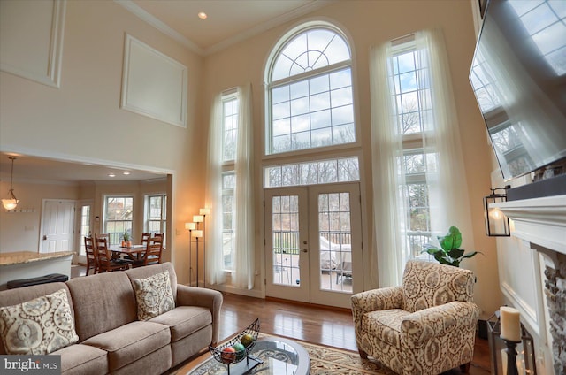 living room with hardwood / wood-style floors, a high ceiling, french doors, ornamental molding, and a fireplace