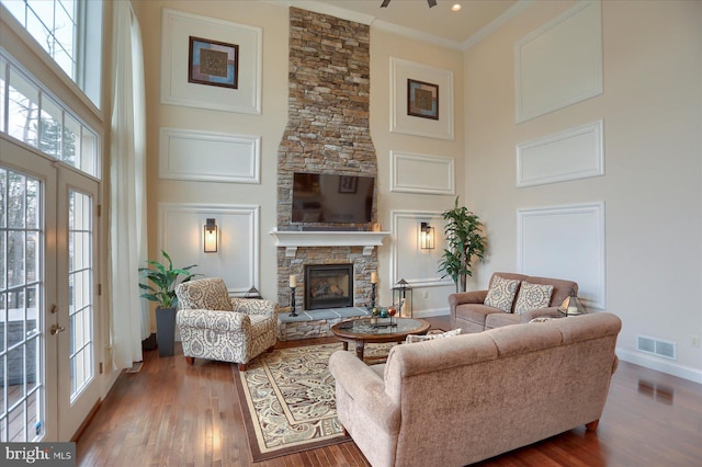 living room with hardwood / wood-style floors, a high ceiling, french doors, crown molding, and a fireplace