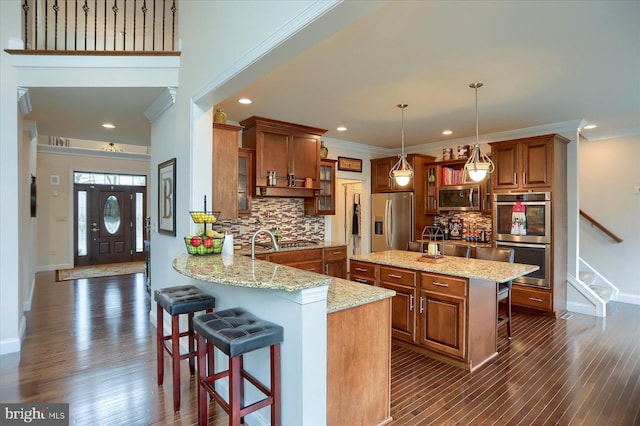 kitchen featuring light stone countertops, stainless steel appliances, kitchen peninsula, pendant lighting, and a breakfast bar