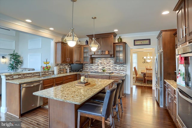 kitchen with pendant lighting, a center island, sink, light stone counters, and stainless steel appliances