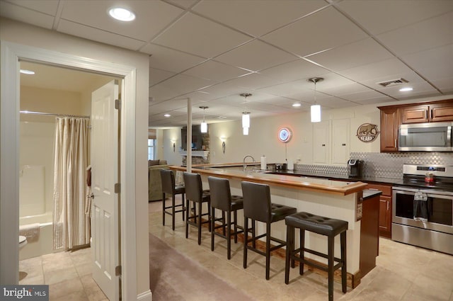 kitchen featuring backsplash, a breakfast bar, stainless steel appliances, decorative light fixtures, and butcher block counters