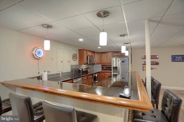 kitchen with sink, hanging light fixtures, stainless steel appliances, kitchen peninsula, and a breakfast bar