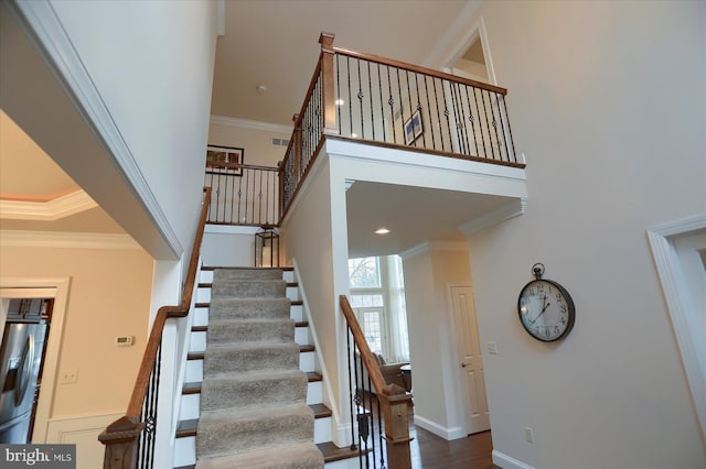 stairway with a towering ceiling, hardwood / wood-style flooring, and ornamental molding