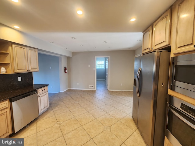 kitchen featuring stainless steel appliances, backsplash, dark stone countertops, light brown cabinetry, and light tile patterned floors