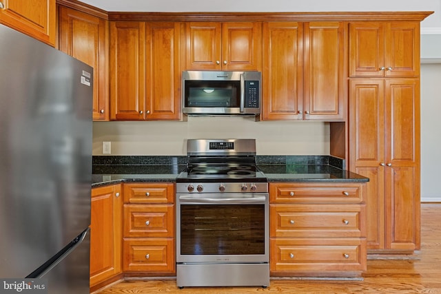 kitchen featuring light wood-type flooring, appliances with stainless steel finishes, and dark stone counters