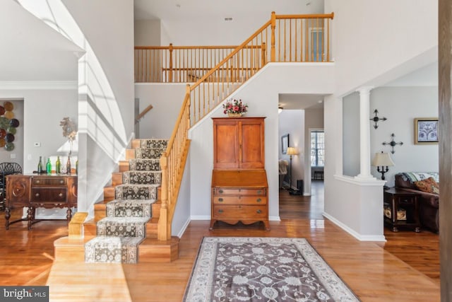 entryway with a high ceiling, hardwood / wood-style flooring, ornate columns, and ornamental molding