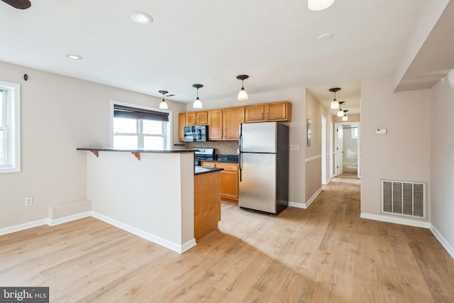 kitchen with pendant lighting, light hardwood / wood-style flooring, a kitchen bar, kitchen peninsula, and stainless steel appliances