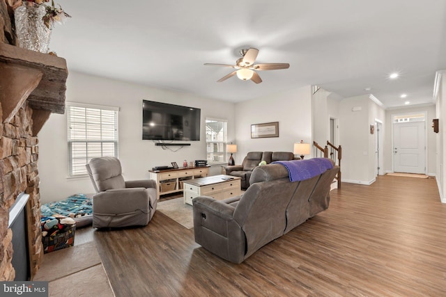 living room featuring ceiling fan, a stone fireplace, and light wood-type flooring