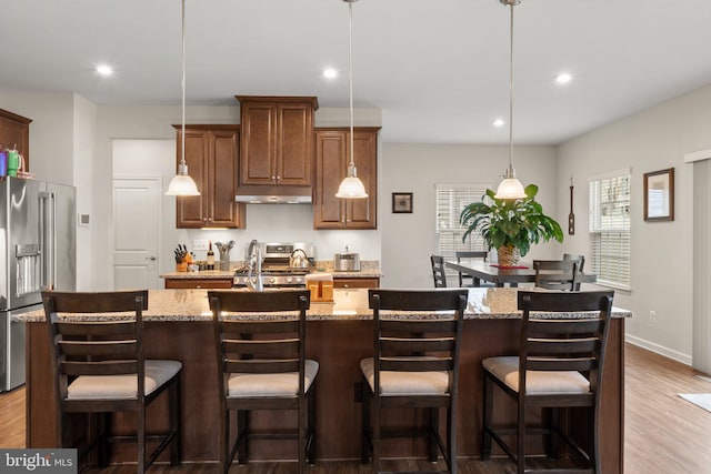 kitchen with stainless steel appliances, light stone countertops, a kitchen breakfast bar, and a spacious island