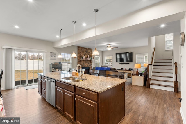 kitchen with sink, dishwasher, hanging light fixtures, light stone countertops, and an island with sink