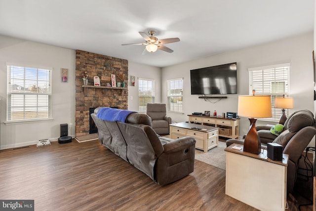 living room featuring ceiling fan, dark hardwood / wood-style flooring, and a stone fireplace