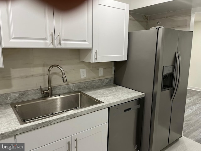 kitchen with appliances with stainless steel finishes, backsplash, sink, light hardwood / wood-style flooring, and white cabinets