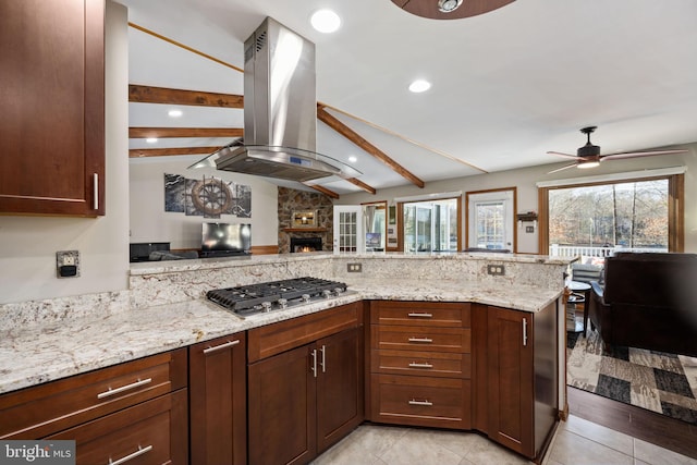 kitchen with stainless steel gas stovetop, vaulted ceiling with beams, ceiling fan, light stone countertops, and island exhaust hood