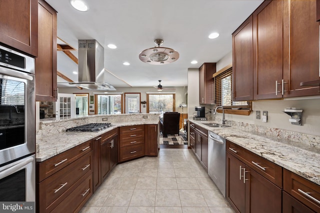 kitchen with ceiling fan, sink, light stone countertops, island exhaust hood, and appliances with stainless steel finishes