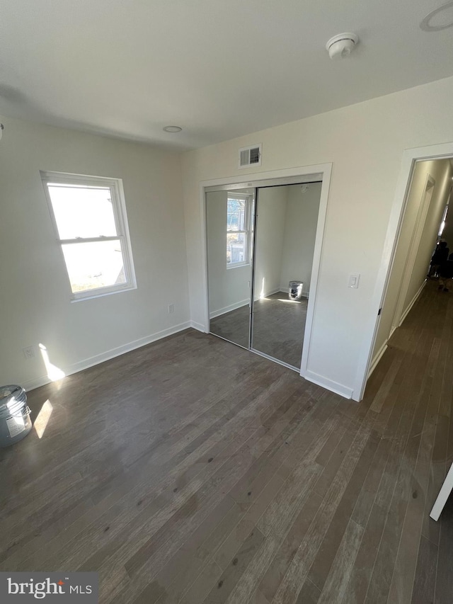 unfurnished bedroom featuring dark wood-style floors, a closet, visible vents, and baseboards