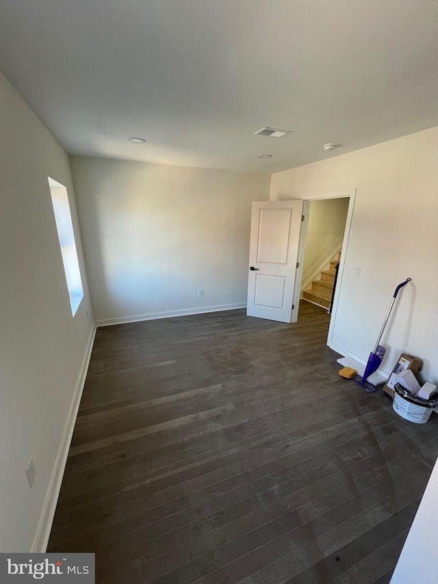 spare room with stairway, baseboards, visible vents, and dark wood finished floors