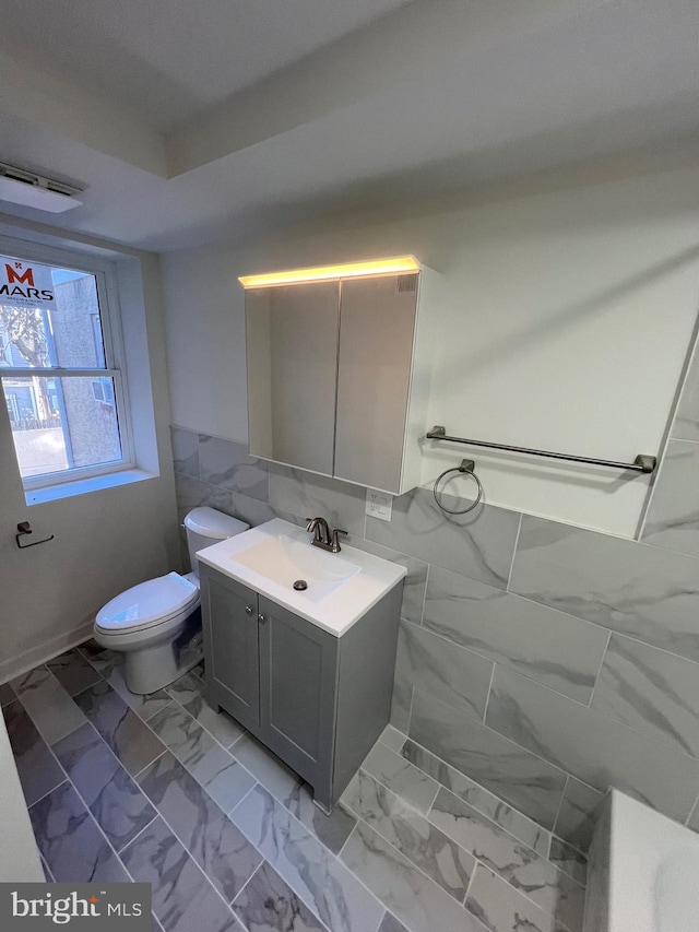 bathroom with toilet, marble finish floor, vanity, and tile walls