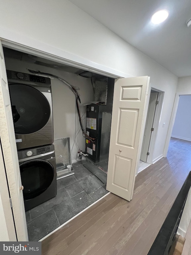 washroom with stacked washer and dryer, wood finished floors, laundry area, and heating unit