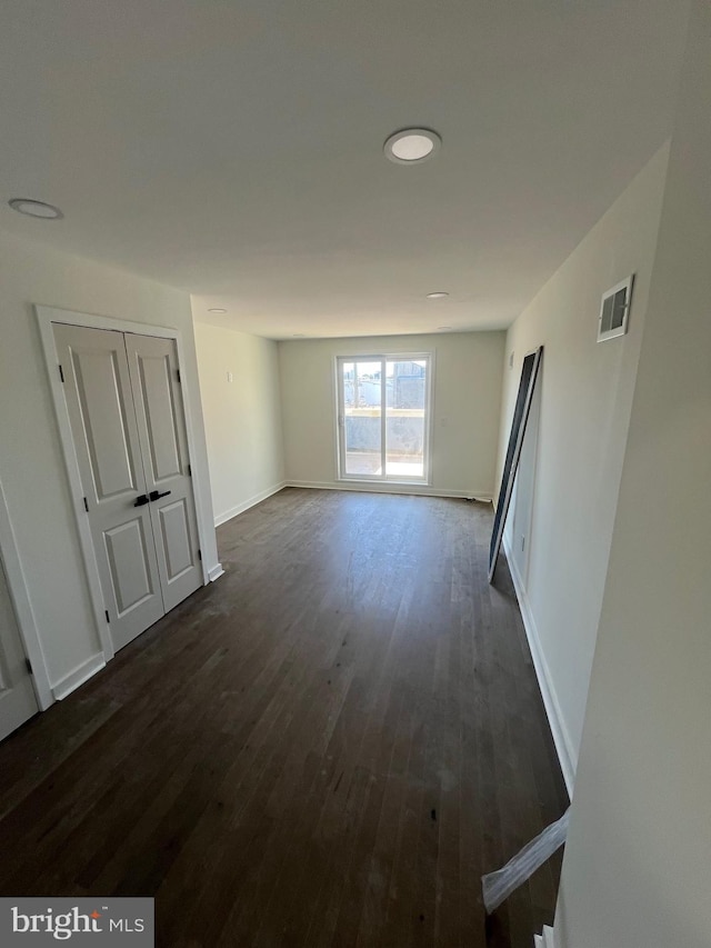 spare room with dark wood-type flooring, visible vents, and baseboards