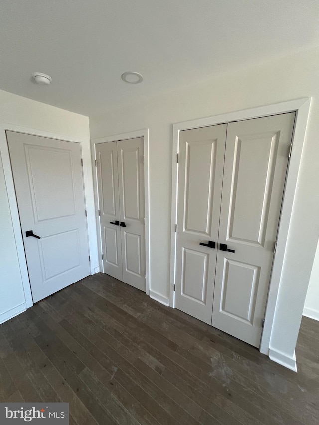 unfurnished bedroom featuring dark wood-type flooring, two closets, and baseboards