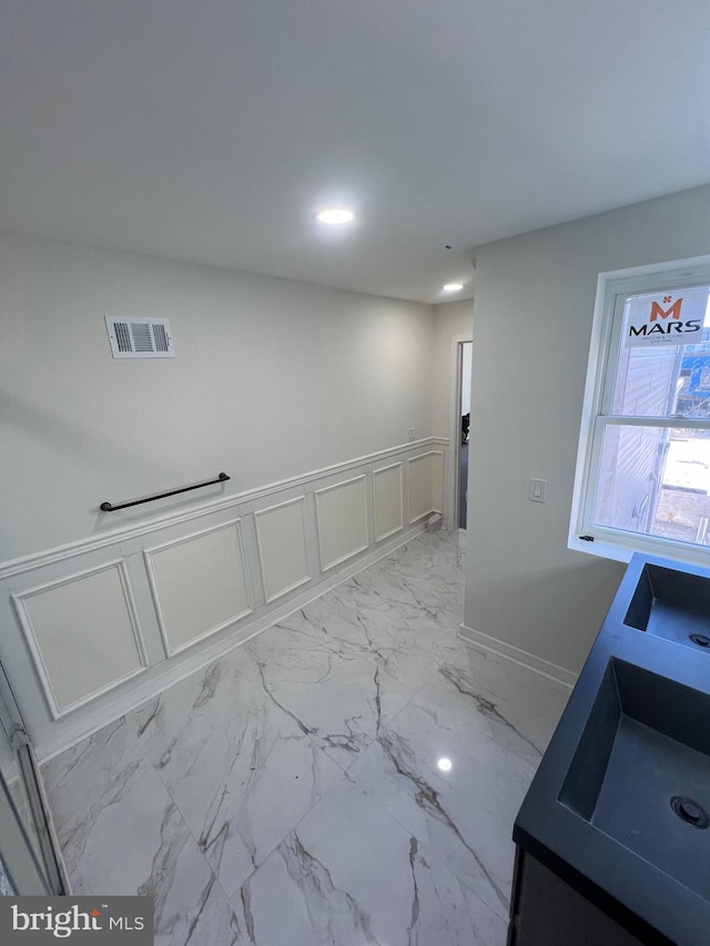 unfurnished room featuring marble finish floor, a wainscoted wall, visible vents, a decorative wall, and a sink