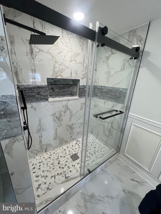 bathroom with marble finish floor, wainscoting, a marble finish shower, and a decorative wall