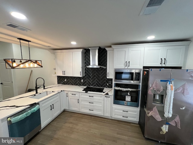 kitchen with stainless steel appliances, wood finished floors, a sink, visible vents, and wall chimney range hood