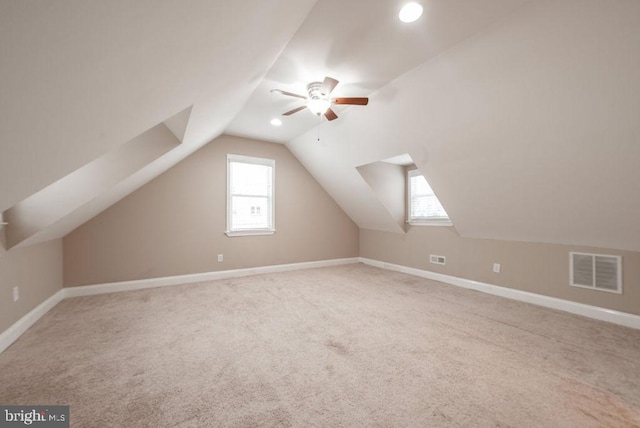 additional living space with ceiling fan, plenty of natural light, light colored carpet, and vaulted ceiling