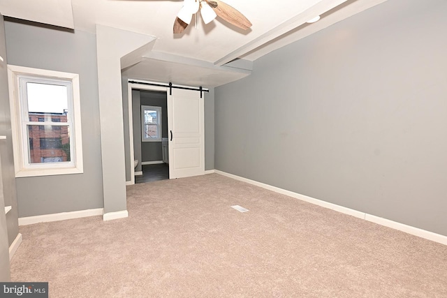 unfurnished bedroom featuring a barn door, ceiling fan, carpet floors, and multiple windows