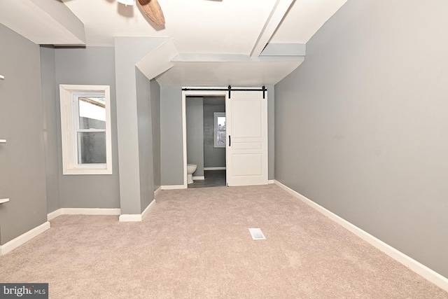 unfurnished bedroom featuring ceiling fan, a barn door, light colored carpet, and ensuite bath