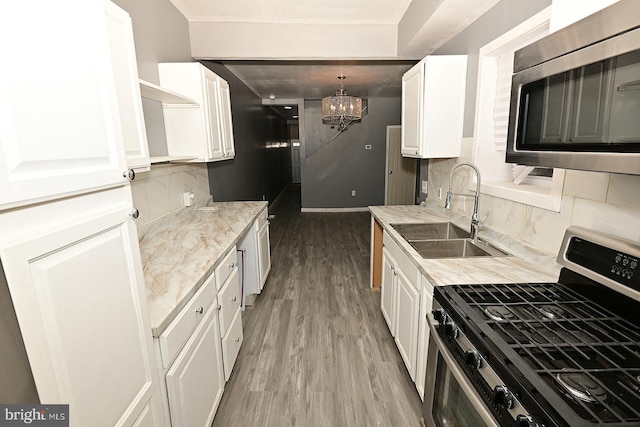 kitchen with appliances with stainless steel finishes, tasteful backsplash, sink, an inviting chandelier, and white cabinetry