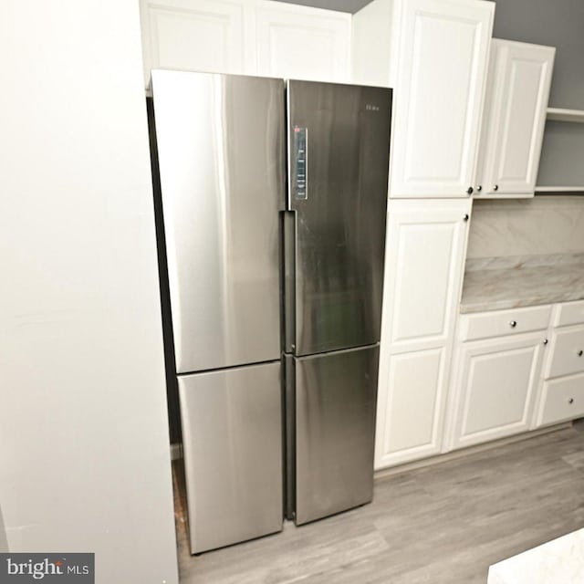 kitchen with light hardwood / wood-style floors, stainless steel fridge, white cabinetry, and backsplash