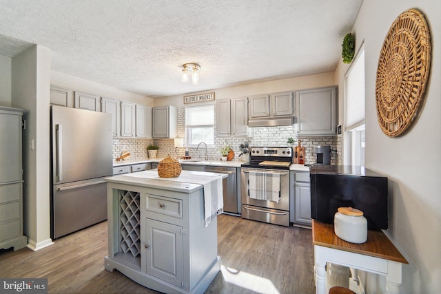 kitchen with stainless steel appliances, a center island, backsplash, dark hardwood / wood-style floors, and gray cabinetry