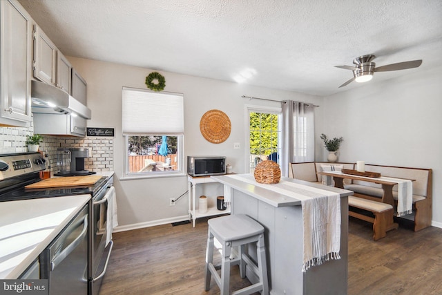 kitchen with stainless steel appliances, a textured ceiling, ceiling fan, a breakfast bar, and dark wood-type flooring