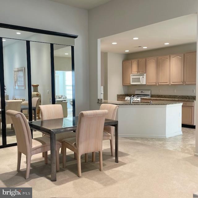 kitchen featuring light brown cabinetry, light colored carpet, and white appliances