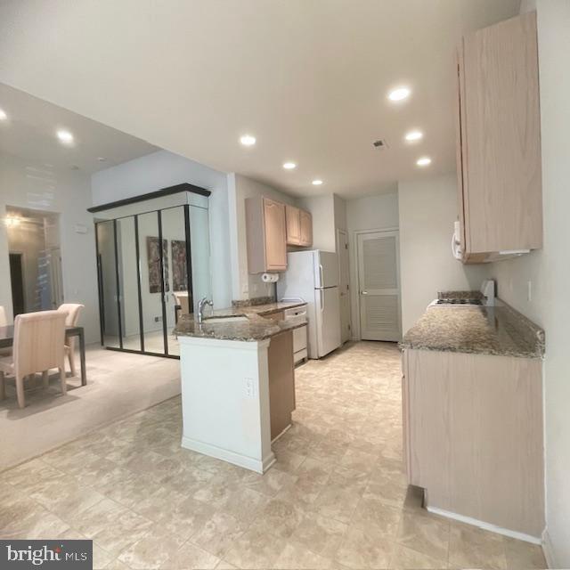 kitchen with white refrigerator, sink, light brown cabinetry, stone countertops, and kitchen peninsula