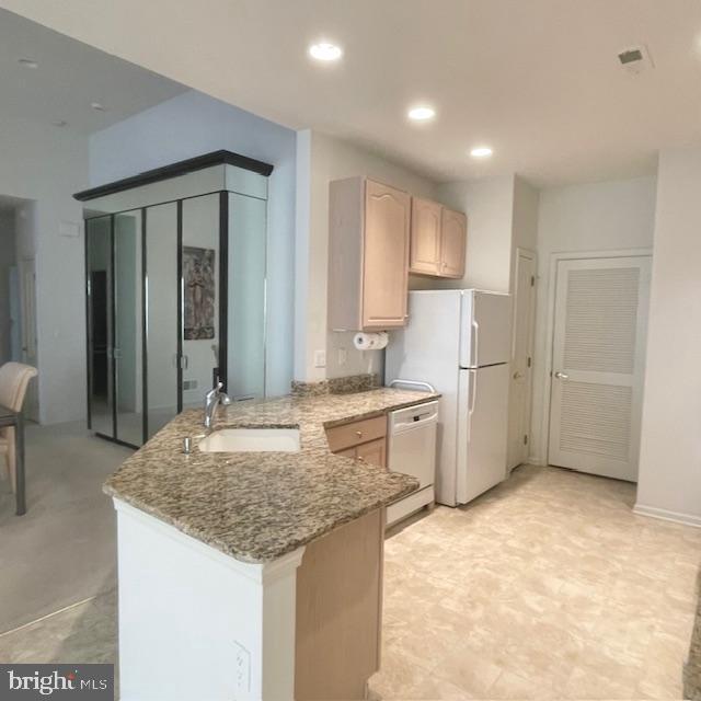 kitchen featuring sink, light stone countertops, light brown cabinetry, dishwashing machine, and kitchen peninsula