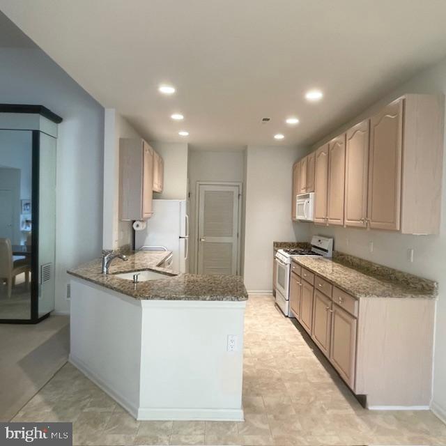 kitchen with kitchen peninsula, dark stone counters, white appliances, sink, and light brown cabinets