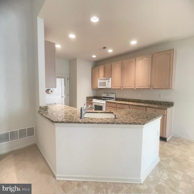 kitchen with sink, light brown cabinets, kitchen peninsula, dark stone counters, and white appliances