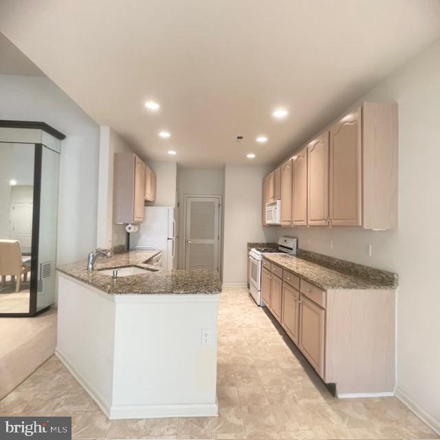 kitchen featuring sink, light brown cabinets, kitchen peninsula, dark stone counters, and white appliances