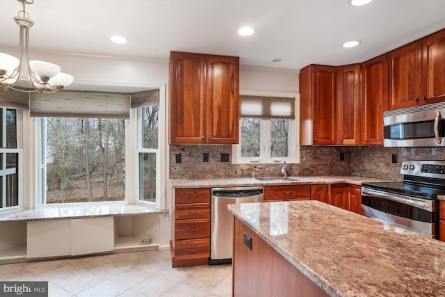 kitchen with appliances with stainless steel finishes, light stone counters, sink, decorative light fixtures, and a notable chandelier