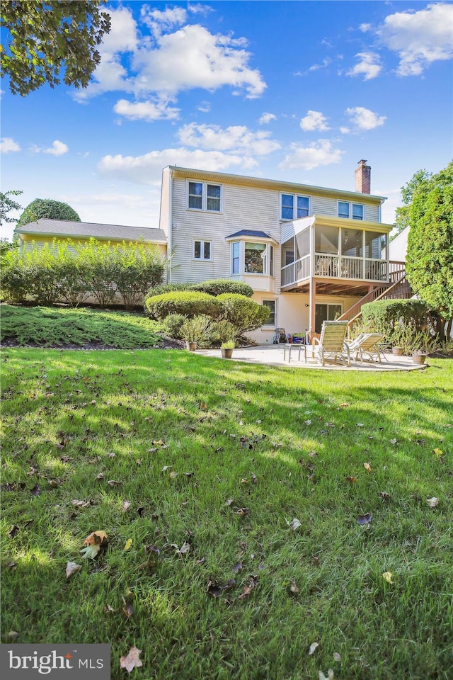 back of property with a sunroom, a patio area, and a lawn