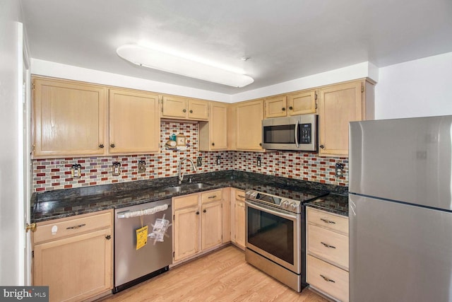 kitchen with light brown cabinets, dark stone countertops, backsplash, and appliances with stainless steel finishes