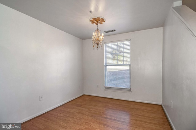 spare room featuring wood-type flooring and an inviting chandelier