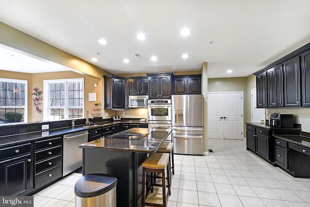 kitchen featuring a center island, stainless steel appliances, dark stone counters, a breakfast bar area, and light tile patterned floors